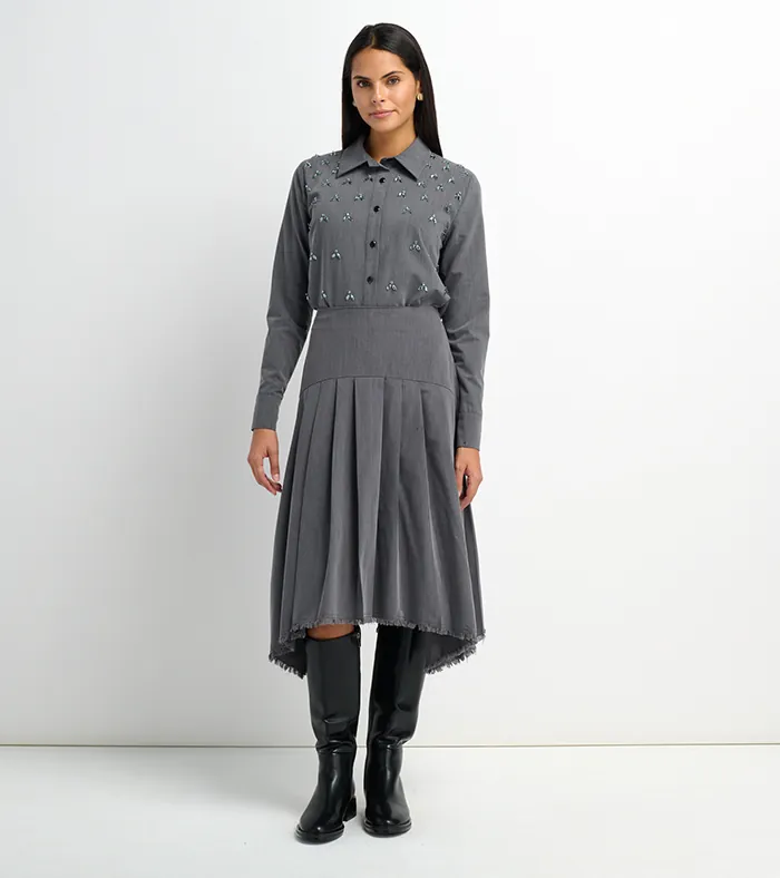 On-model photography of a grey embellished shirt and asymmetric pleated skirt with black boots