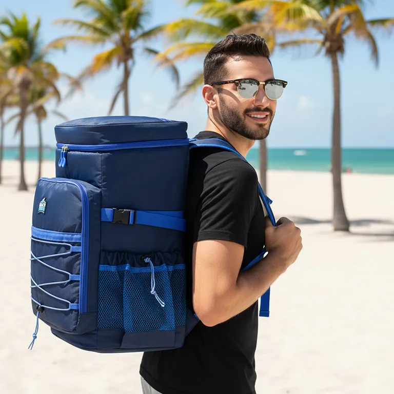 Lifestyle image of a man carrying a navy cooler backpack on a beach with palm trees