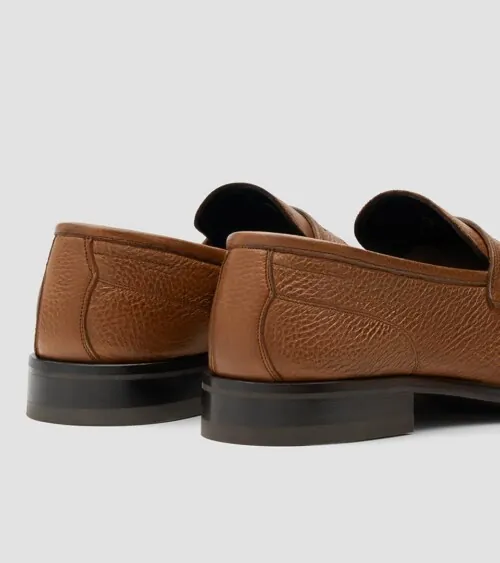 Pair of cognac pebbled leather penny loafers from the back at three-quarter angle on grey background, studio product photography