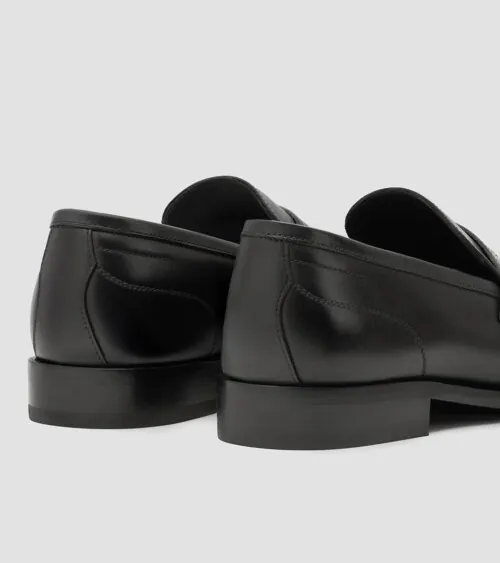 Pair of black leather penny loafers photographed from the back at three-quarter angle on grey background, footwear product photography