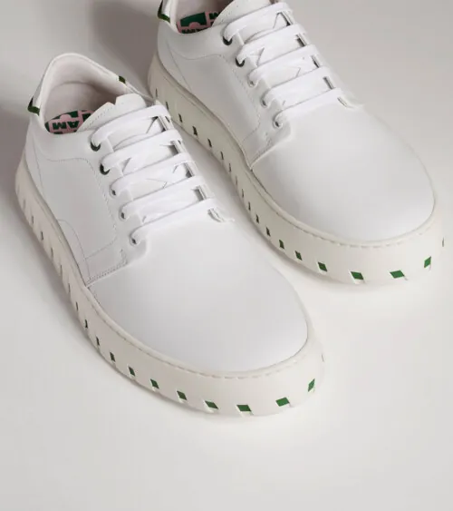 Pair of white leather low-top platform sneakers shown at three-quarter angle on grey background, footwear product photography
