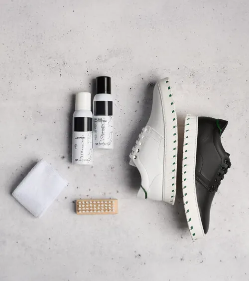 White sneaker styled flat lay with shoe-care cleaner, cloth, and brush on concrete surface, lifestyle product photography