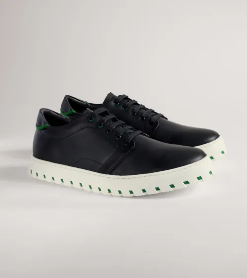 Black leather low-top sneaker with white platform sole shown in side profile on grey background, footwear product photography