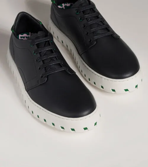 Pair of black leather low-top sneakers with white platform soles at three-quarter angle on grey background, studio product photography