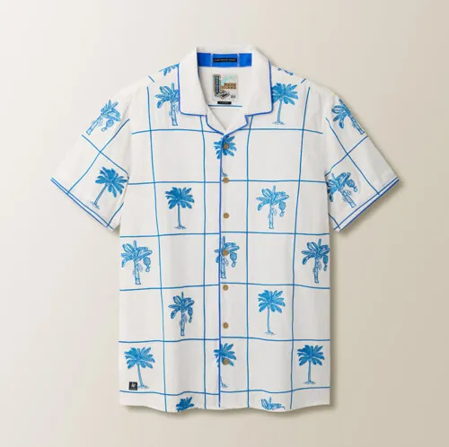 Flat lay photography of a white tropical print button-down shirt with blue palm tree pattern.