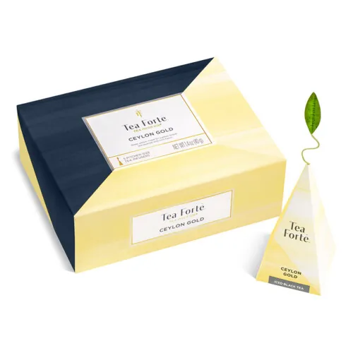 Product photography of a closed yellow and navy tea box next to a pyramid tea sachet