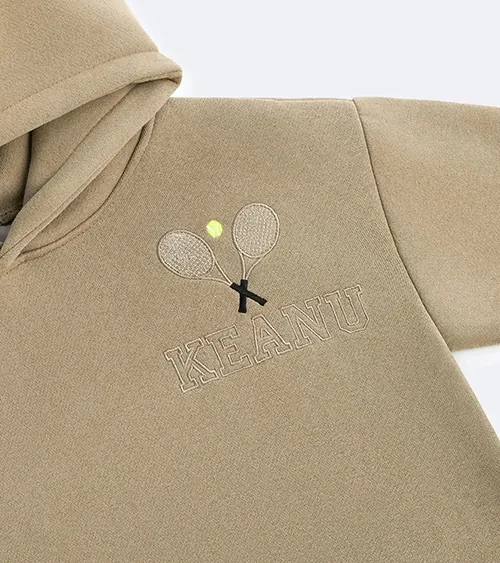 Flat lay detail photography showing embroidered logo on a beige children's hoodie for apparel product photography by Shootify.