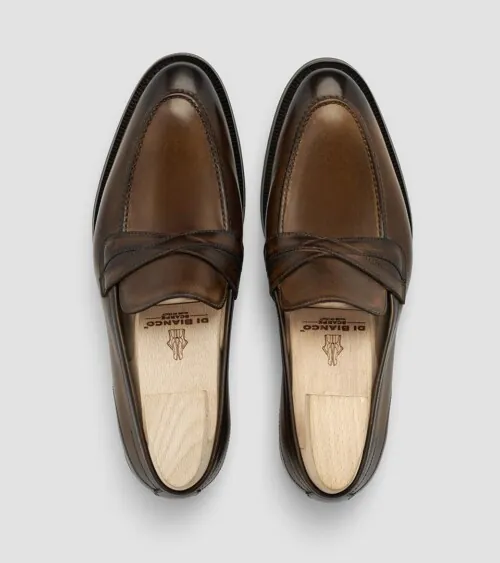 Pair of brown burnished leather penny loafers with shoe trees photographed top-down on grey background, studio product photography