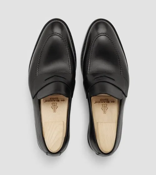 Pair of black leather penny loafers with shoe trees photographed top-down on grey background, footwear product photography