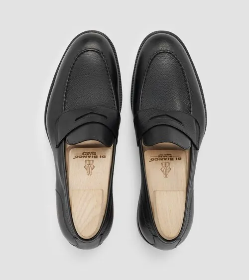 Pair of black pebbled leather penny loafers with shoe trees photographed top-down on grey background, studio product photography