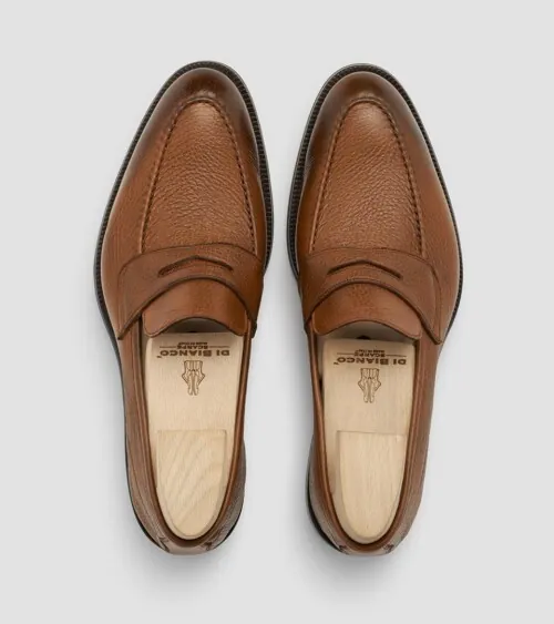Pair of cognac leather penny loafers with shoe trees photographed top-down on grey background, footwear product photography