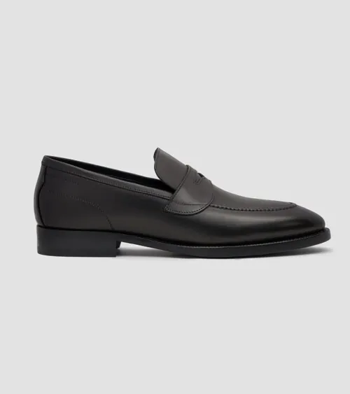 Single black leather penny loafer in side profile on grey background, footwear product photography