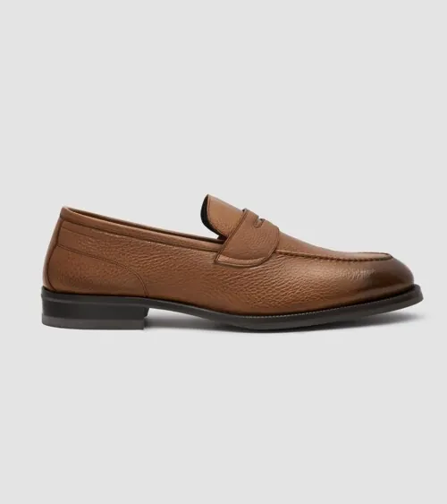 Single tan pebbled leather penny loafer shown in side profile on grey background, studio product photography