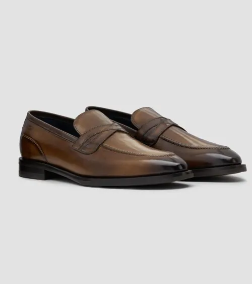 Pair of brown burnished leather penny loafers at three-quarter front angle on grey background, studio product photography
