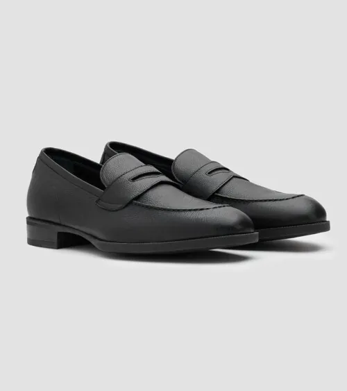 Pair of black leather penny loafers at three-quarter front angle on grey background, footwear product photography