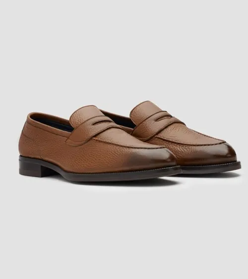 Pair of cognac pebbled leather penny loafers at three-quarter front angle on grey background, studio product photography