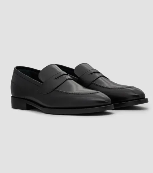 Pair of black leather penny loafers shown at three-quarter front angle on grey background, footwear product photography
