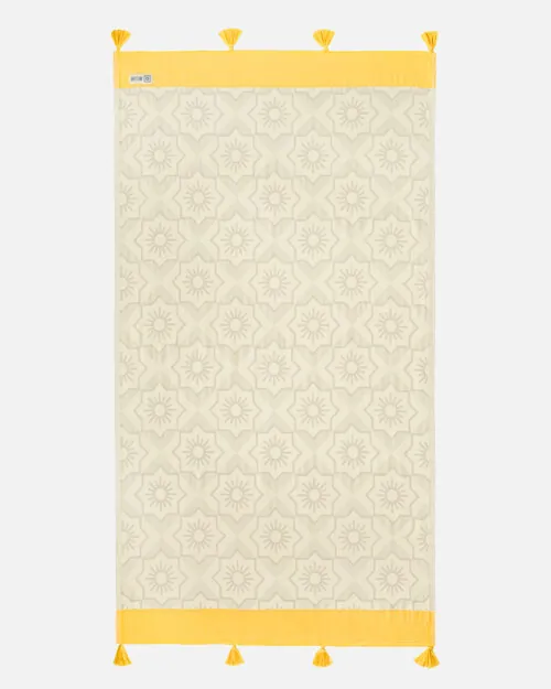 Flat lay photography of a cream towel with a tonal sun-medallion weave and yellow tasselled border, shown full length