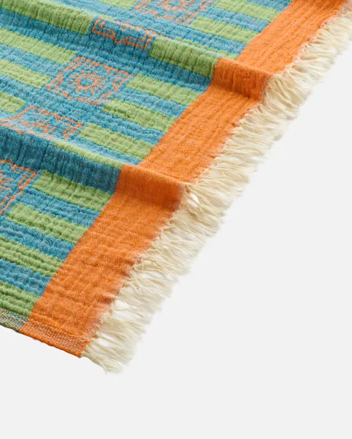Close-up product photography of the fringed corner of a green and blue striped towel with an orange band