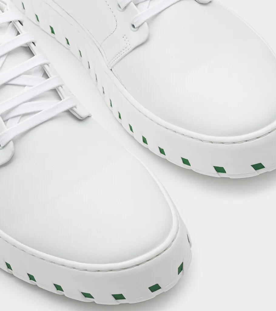 Shoe product photography of a white leather lace-up shoe in close-up crop showing the ridged white sole with green inserts