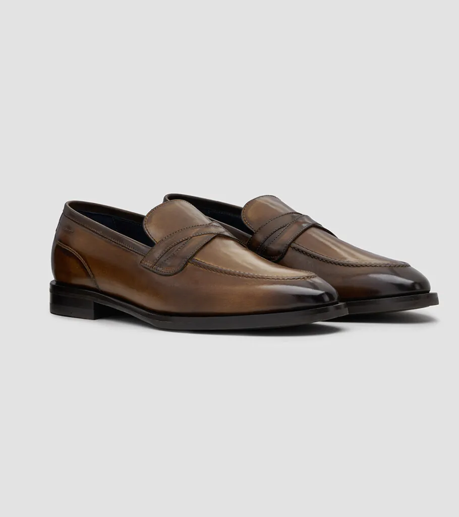 Shoe product photography of a pair of burnished tan penny loafers at a front three-quarter angle