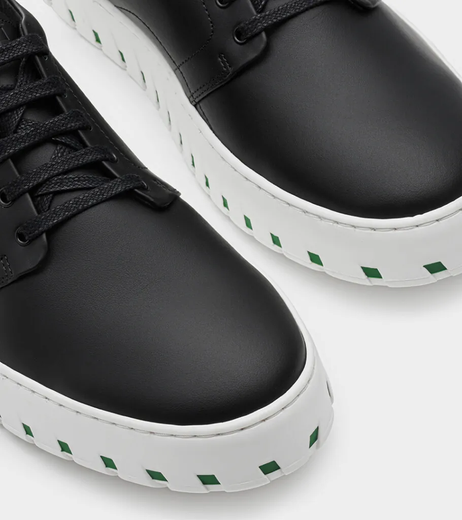 Shoe product photography of a black leather lace-up shoe in close-up crop showing the toe and white ridged platform sole
