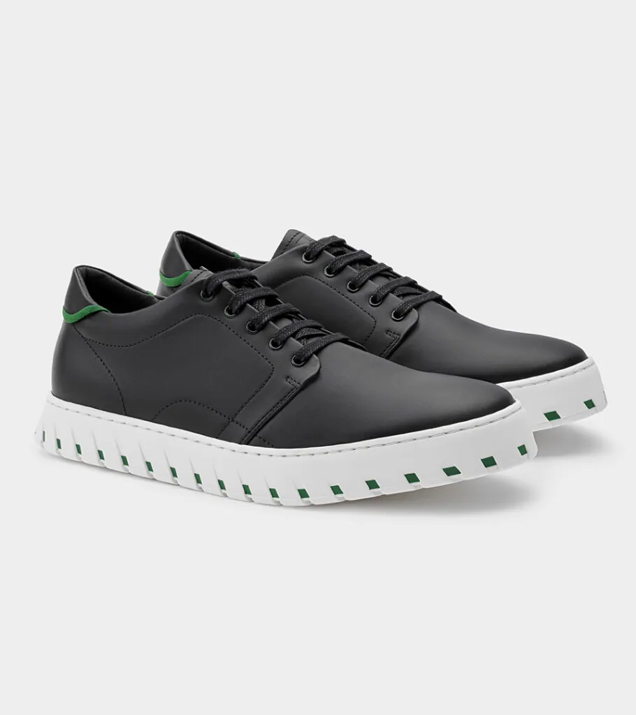 Shoe product photography of a black leather lace-up sneaker at a front three-quarter angle with a white ridged sole