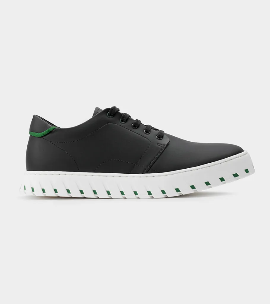 Shoe product photography of a black leather sneaker in side profile with a white ridged platform sole and green heel loop