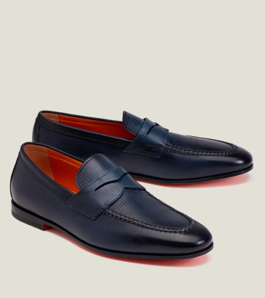 Shoe product photography of a pair of navy leather penny loafers at a front three-quarter angle with orange leather linings