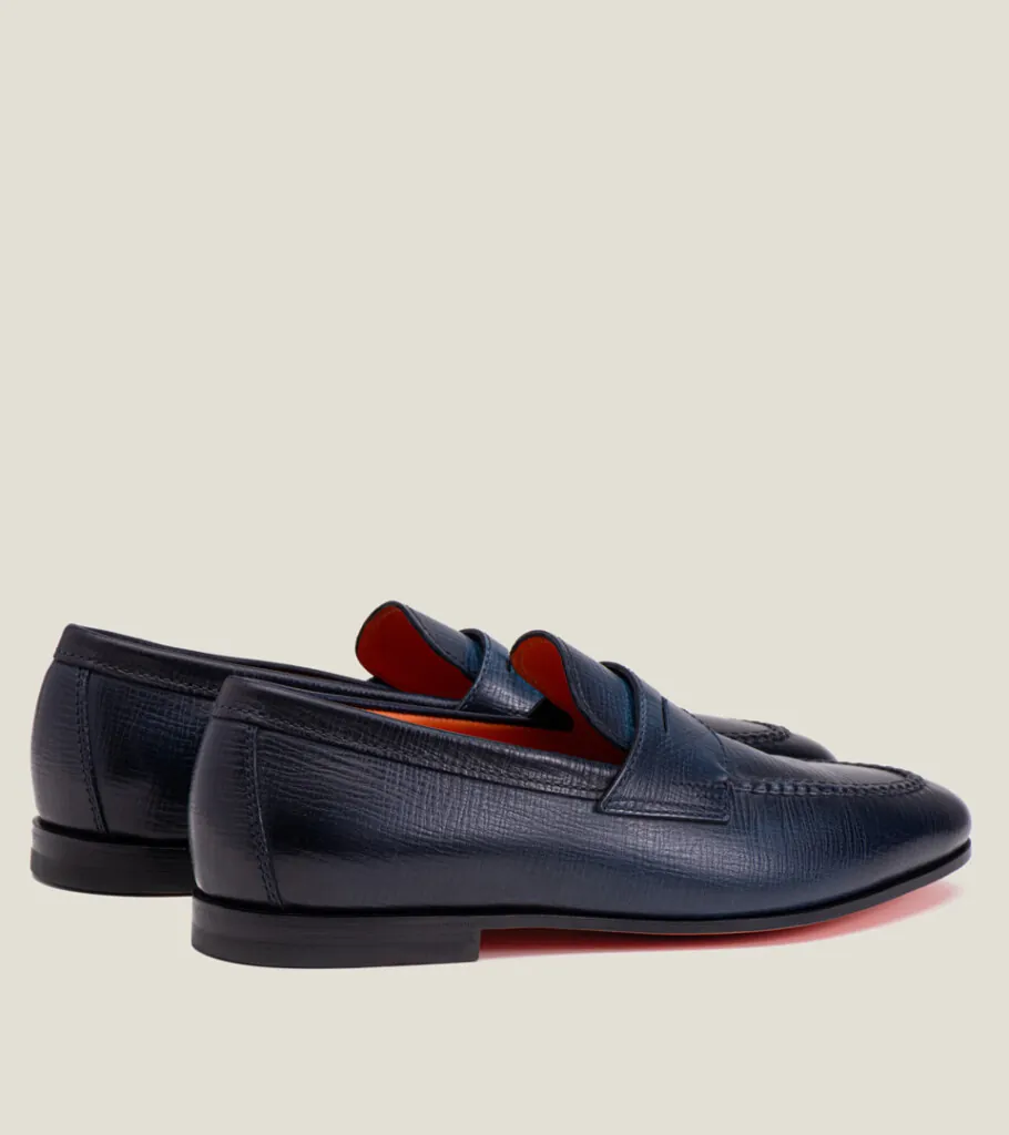 Shoe product photography of a pair of navy penny loafers viewed from behind showing heel counters and orange sole edges