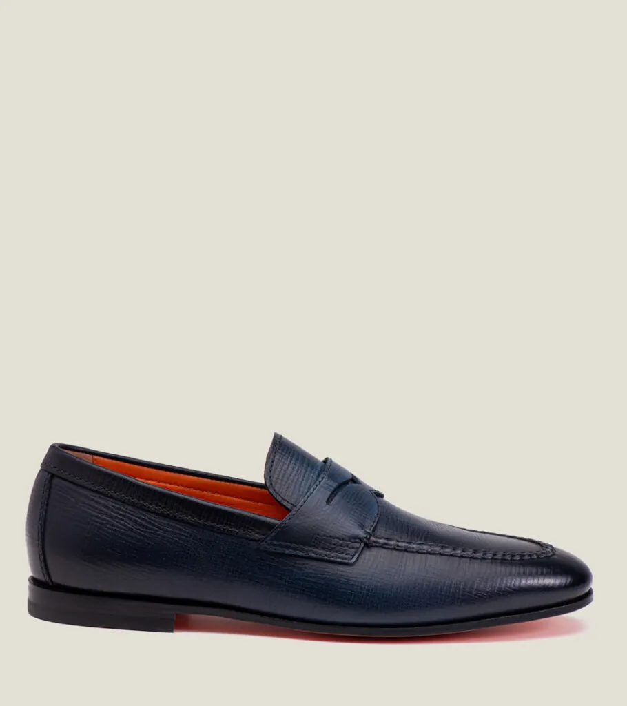 Shoe product photography of a navy leather penny loafer in side profile with a dark sole and orange edge trim