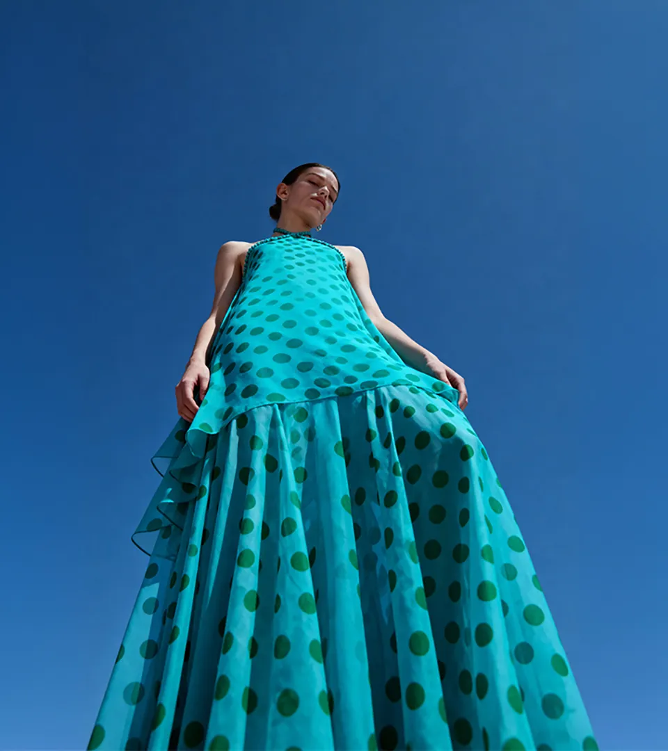 fashion model in teal polka-dot gown photographed from low angle against bright blue sky