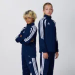 Two teen models in matching navy adidas tracksuits with white stripes
