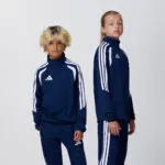 Two teen models in matching navy adidas tracksuits, side view