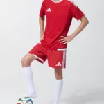 Male model in red soccer jersey and shorts with foot resting on a soccer ball