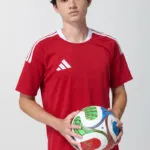 Male model in red adidas soccer jersey holding a soccer ball