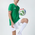Male model in green soccer jersey balancing a soccer ball on his foot