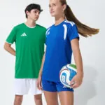 Two youth models in green and blue soccer jerseys holding a soccer ball together